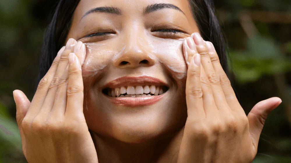 Woman smiling with eyes closed while applying natural Ua Body skincare, highlighting the clean beauty benefits of Hawaiian-made products like Pikake Jasmine Mist.